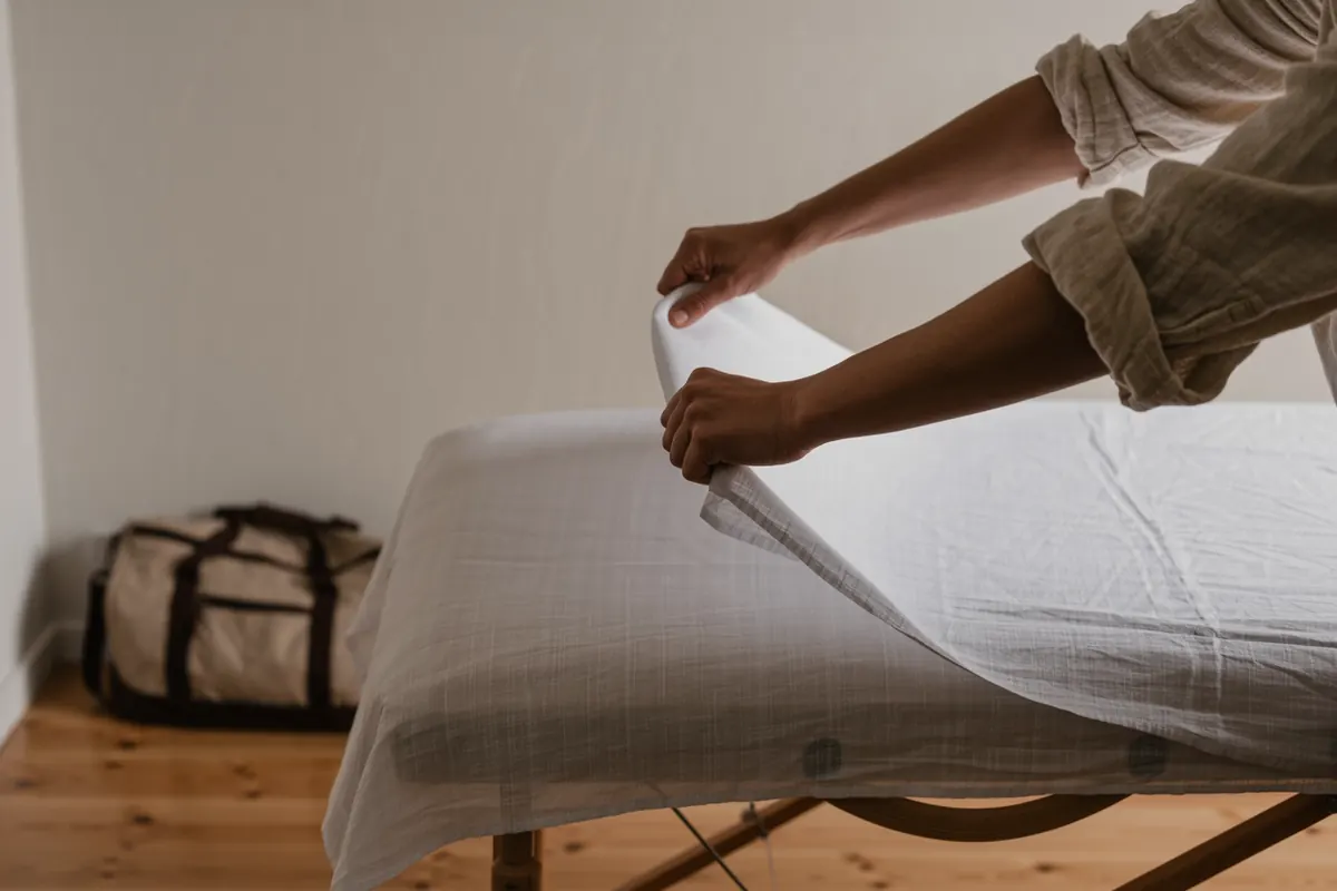 Praticienne dépliant un drap sur sa table de massage installée dans une salle de club sportif