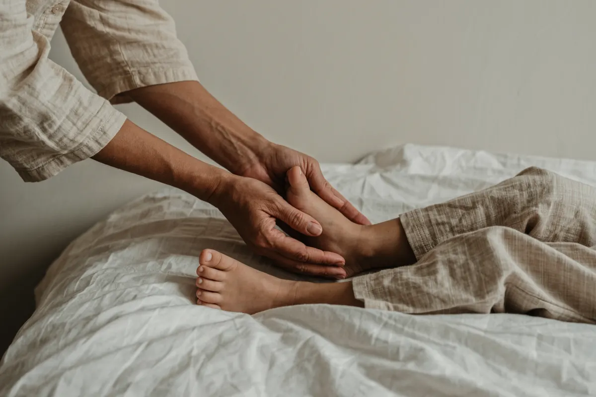Mains d'une praticienne enveloppant le pied d'un enfant pour l'apaiser avant le coucher