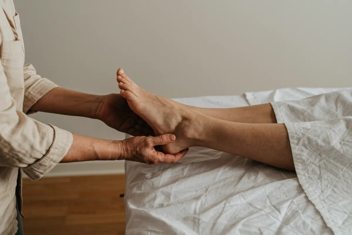 Pieds nus entre les mains d'une praticienne, sur une table de massage dressée de lin blanc
